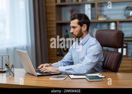 A focused and serious young man is working in the office on a laptop on a project, copying, analyzing data and information. Stock Photo
