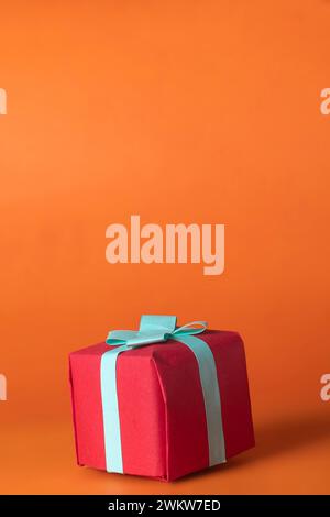 Red gift box with blue bow isolated on orange background. Copy space Stock Photo