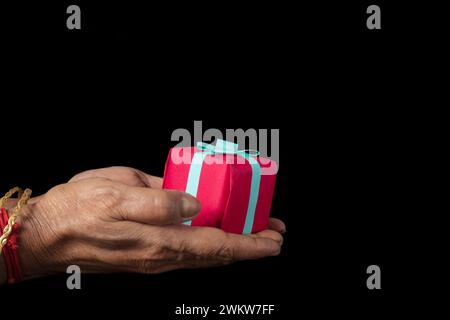 Close up shot of Indian female hands holding a small gift box on a black background. Stock Photo