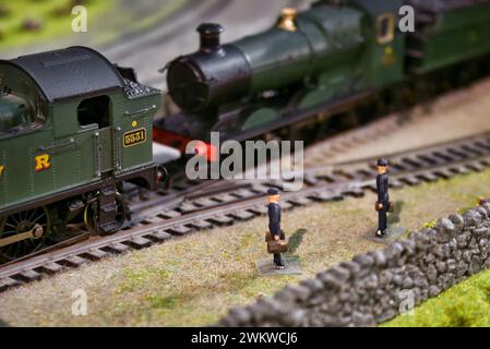 Close-up shot of miniature figures next to a model train track with detailed old-fashioned steam engine locomotives Stock Photo