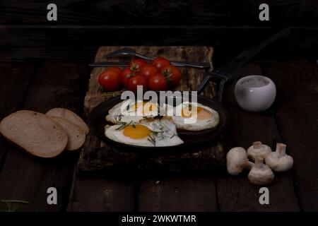 Fried eggs in a pan with vegetables and herbs on a black background Stock Photo