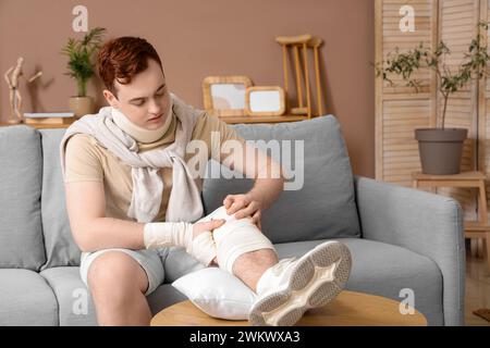 Injured young man after accident with his leg on pillow at home Stock Photo