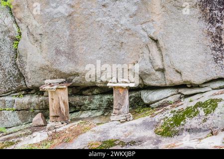 Two logs held in place with stones and carved to have one eye and mouth on rocky ledge of cliff face in countryside in South Korea Stock Photo