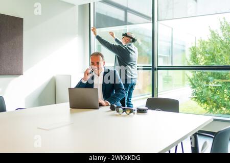 Businessman working using laptop while a colleague is using VR googles in the office Stock Photo