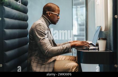 Focused young man with glasses working on a laptop in a modern coworking office. Business man typing diligently inside his booth, creating a professio Stock Photo