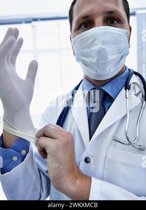 Portrait, doctor and man putting on gloves for safety or protection in hospital. Face mask, medical professional or ppe to prepare for surgery Stock Photo