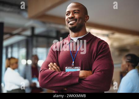 Business man stands confidently with arms crossed, wearing a badge. His smile denotes success and approachability, illustrating a positive business en Stock Photo