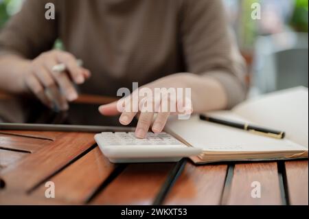 A close-up shot of a woman using a calculator, calculating her salary and monthly expenses at a table in a cafe. financial, budget, income Stock Photo