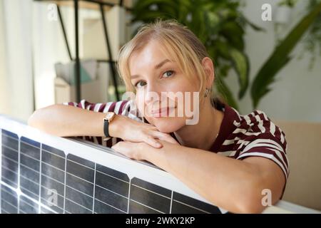 Portrait of woman leaning on solar panel and smiling at camera Stock Photo