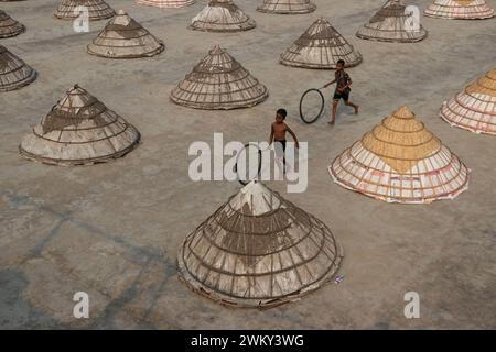 Brahmanbaria, Chittagong, Bangladesh. 23rd Feb, 2024. Children play among hundreds of giant hat-shaped bamboo cones in a rice field in Brahmanbaria, Bangladesh. This is a traditional method of keeping freshly collected rice protected from rain and fog after the removal of moisture. The dried rice is piled into cone-shaped mounds so that it fits under the cones. The rice mill worker start their work very early in the morning from 5 am and work till 2 pm every day. After that, the Children of the workers play their afternoon games. (Credit Image: © Joy Saha/ZUMA Press Wire) EDITORIAL USAGE ON Stock Photo