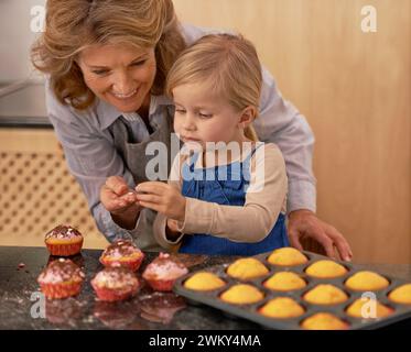 Grandmother, child and baking cupcakes or decorating with icing or learning creativity, bonding or teamwork. Female person, girl and sweet treats or Stock Photo