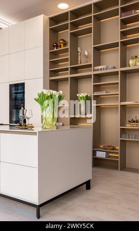 A modern, chic kitchen featuring stylish white cabinets, kitchen island and illuminated shelves Stock Photo