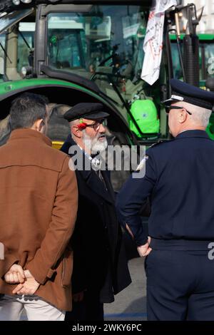 An old man with white beard, black cap and a carnation flower at the back of his ear is talking to a fellow man and a police officer during a protest Stock Photo