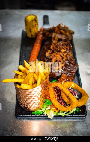 Steak, onions rings, fries, corn on the cob, sausage and salad prepared in a kitchen. Stock Photo