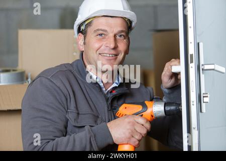 male locksmith using a cordless screwdriver on a door lock Stock Photo
