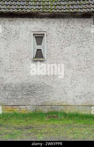 Gray exterior wall with washed plaster and a small window made of glass blocks Stock Photo