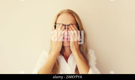 Tired overworked middle-aged woman employee rubbing her eyes suffering from eye strain, dry eye syndrome or headaches after working at the computer Stock Photo