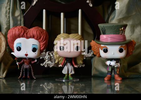 Funko Pop action figures of Mad Hatter, Red Queen and Alice in Wonderland. Palace, teapot, reflection floor, green curtain, fabulous, fantasy, moody. Stock Photo