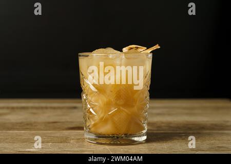 A cocktail with a slice of dried banana and ice on a wooden table Stock Photo