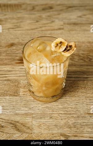 A cocktail with a slice of dried banana and ice on a wooden table Stock Photo