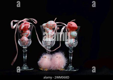 Pink and white easter eggs in glasses. Pink fluffy easter chicks on a table. Stock Photo
