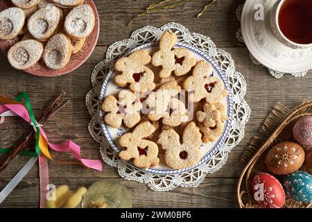 Homemade Linzer cookies in the shape of animals on a plate, with Easter eggs decorated with wax, top view Stock Photo