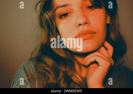 Woman in black and orange outfit, hand on chin, posing against wall Stock Photo