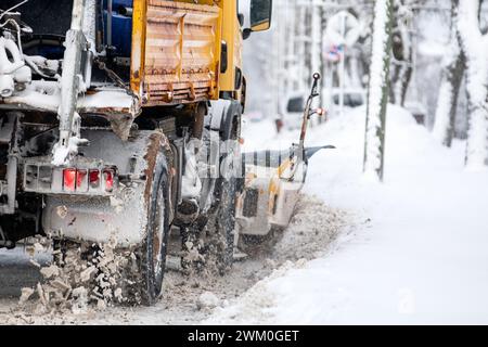 A snow-covered snowplow cleans the street after a snowfall, viw from back. Stock Photo