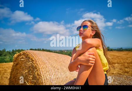 Girl sitting on hay bale in field Stock Photo