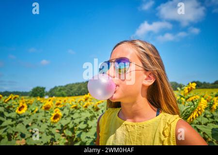 Girl blowing bubble gum in sunflower field on sunny day Stock Photo