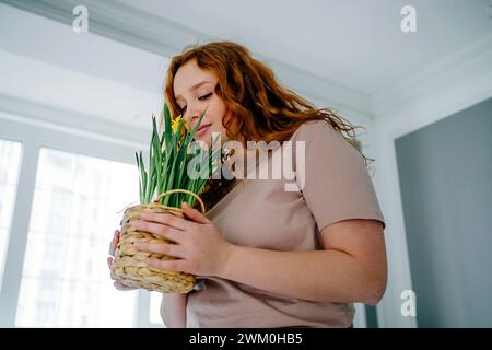 Redhead woman smelling daffodil flower at home Stock Photo