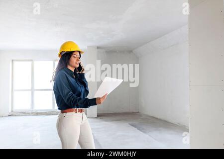 Architect having discussion over blueprint on mobile phone at site Stock Photo