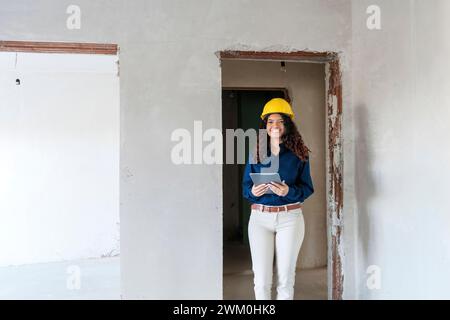 Happy architect wearing yellow hardhat and standing with tablet PC at site Stock Photo