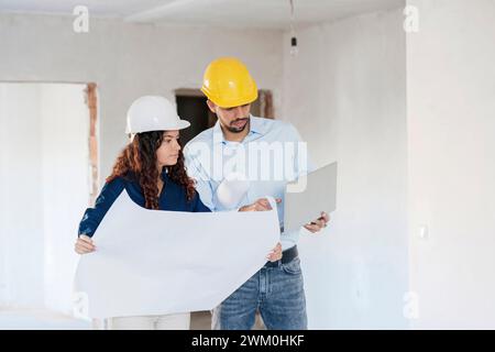 Architects with blueprint discussing over laptop at site Stock Photo