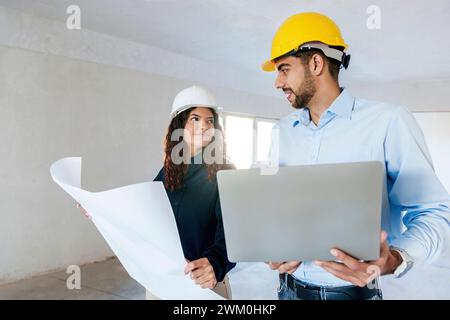 Smiling architects discussing with blueprint and laptop at site Stock Photo