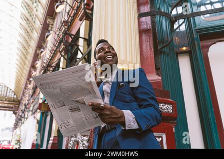 Happy mature businessman with newspaper talking on smart phone Stock Photo