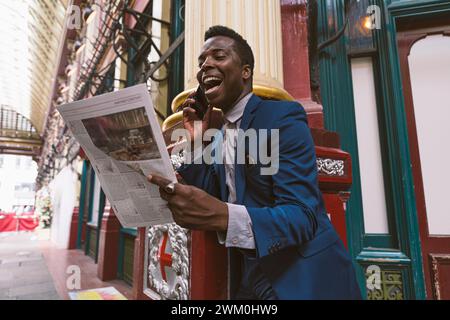 Happy businessman reading newspaper and talking on smart phone Stock Photo