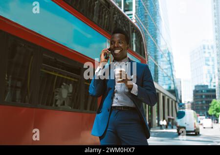 Smiling businessman talking on smart phone near bus on street Stock Photo