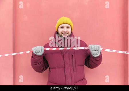 Happy man holding red and white barricade tape in front of peach wall Stock Photo