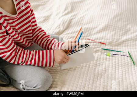 Girl putting colored pencils in pouch on bed at home Stock Photo