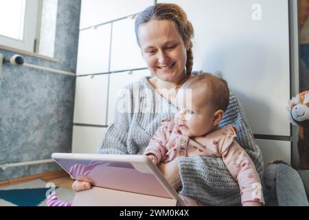 Cute baby girl with mother using tablet PC at home Stock Photo