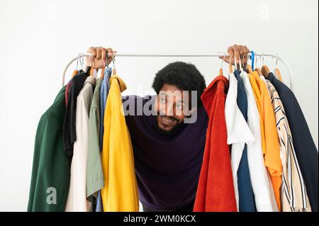 Happy young man looking through clothes rack at home Stock Photo