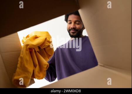 Smiling young man putting clothes in cardboard box Stock Photo