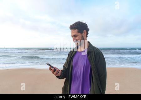 Smiling man using mobile phone at beach Stock Photo
