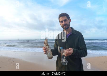 Man standing with plastic bottles under cloudy sky at beach Stock Photo