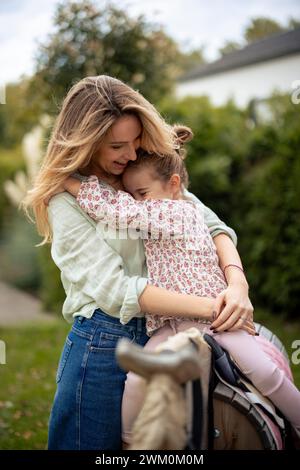 Girl sitting on wooden horse and hugging happy mother in garden Stock Photo