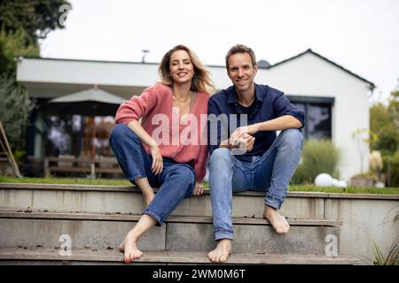 Happy man sitting with woman in front of house Stock Photo