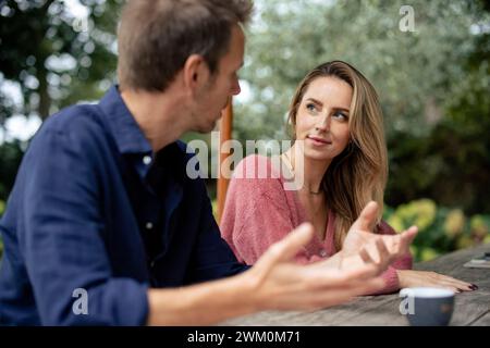 Man talking to woman sitting at table in garden Stock Photo