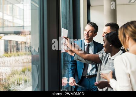 Happy business colleagues discussing over document on window at office Stock Photo