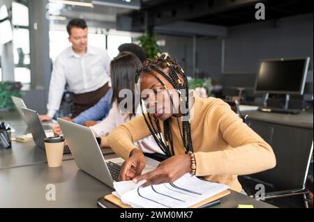 Businesswoman examining documents with colleagues discussing in background Stock Photo